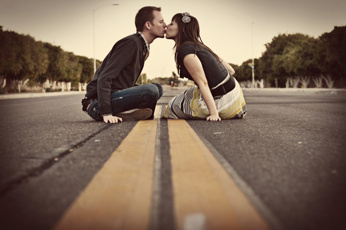 Couple sitting on the yellow lines in the road kissing for a cute couple picture. 
