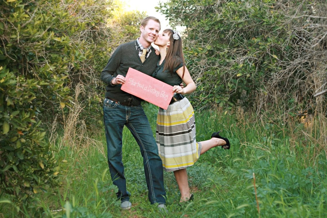 Couple with wife kissing husband\'s cheek hodling up a sign that says Highlights of the first year of marriage. 