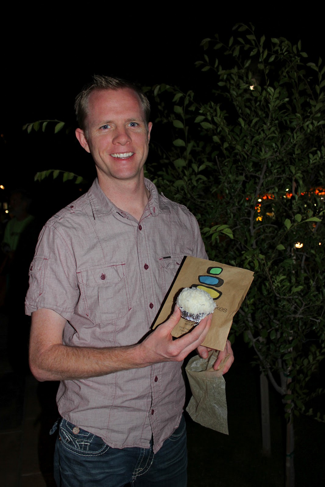 A man holding Tammie Coe cupcakes outside the shop at night. 