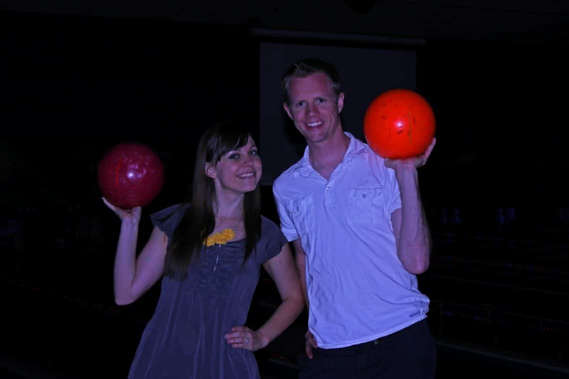 A couple on a bowling date night holding up their bowling balls. 