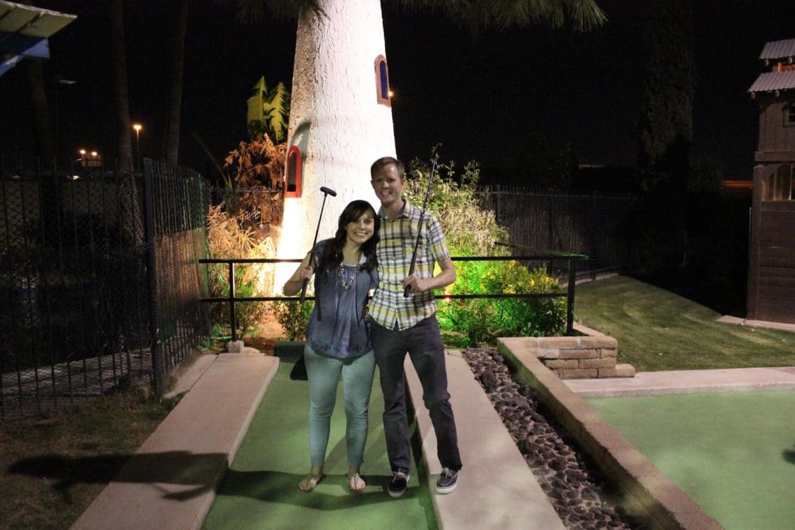 Couple on a mini golf course smiling on their miniature golfing date night. 