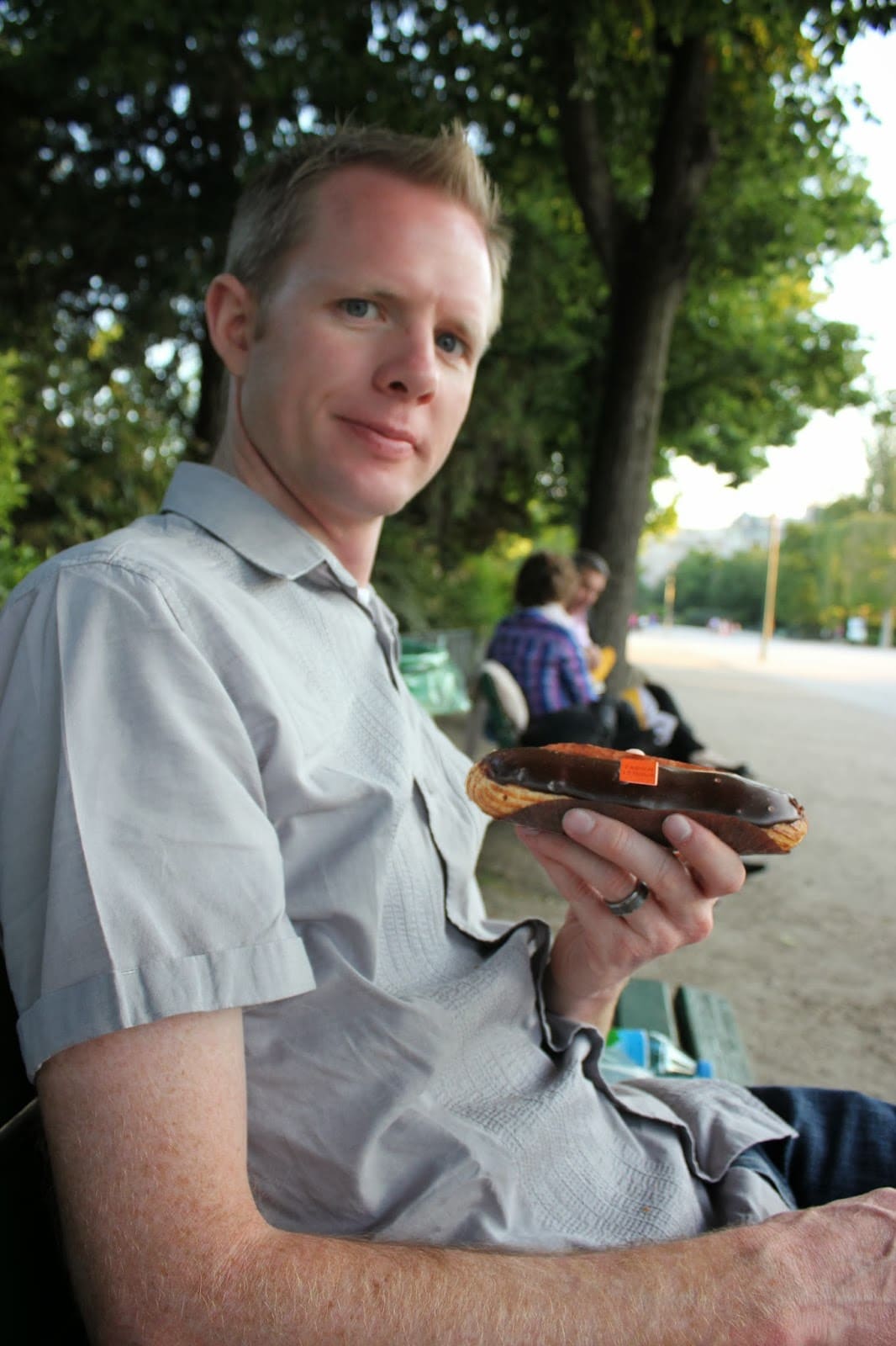 Man holding a pastry on a park bench by the Eiffel Tower. 