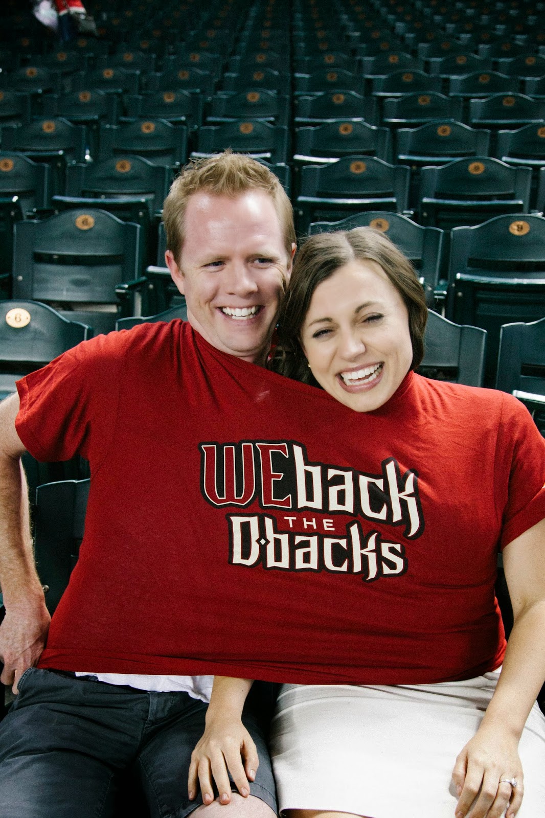 A couple both wearing a free shirt from a baseball game. 