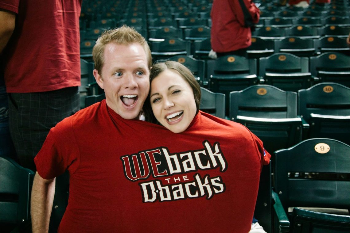 A couple both wearing the same shirt showing how large free shirts at baseball games are. 