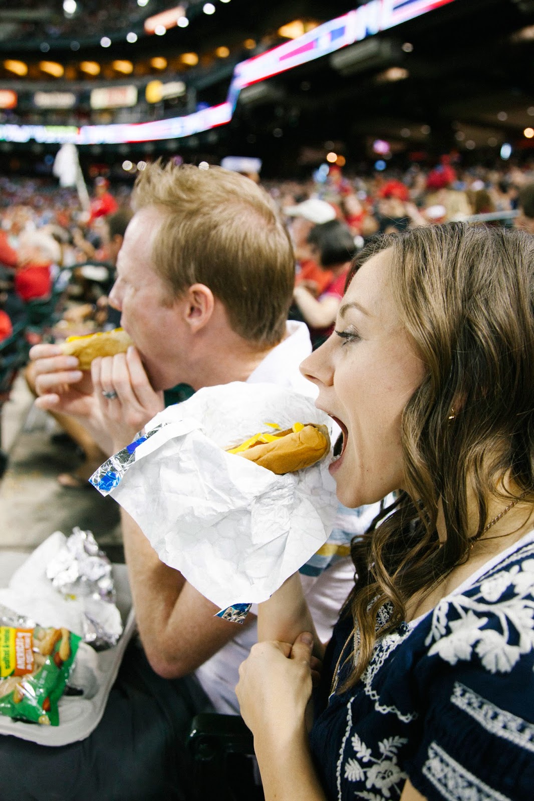 A couple enjoying hot dogs during a Baseball date night. 