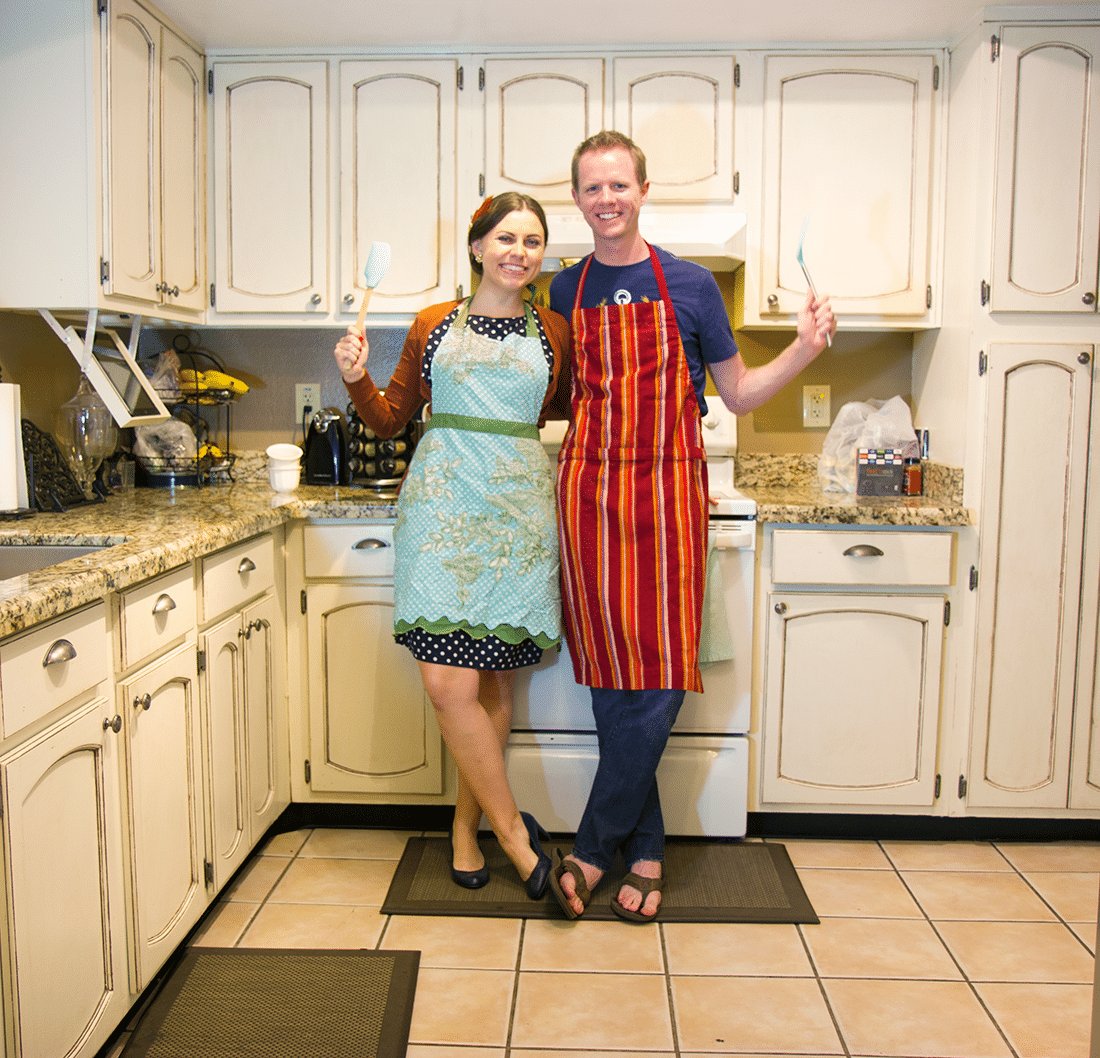 Couple standing in their kitchen holding cooking tools ready for a cooking date night at home. 