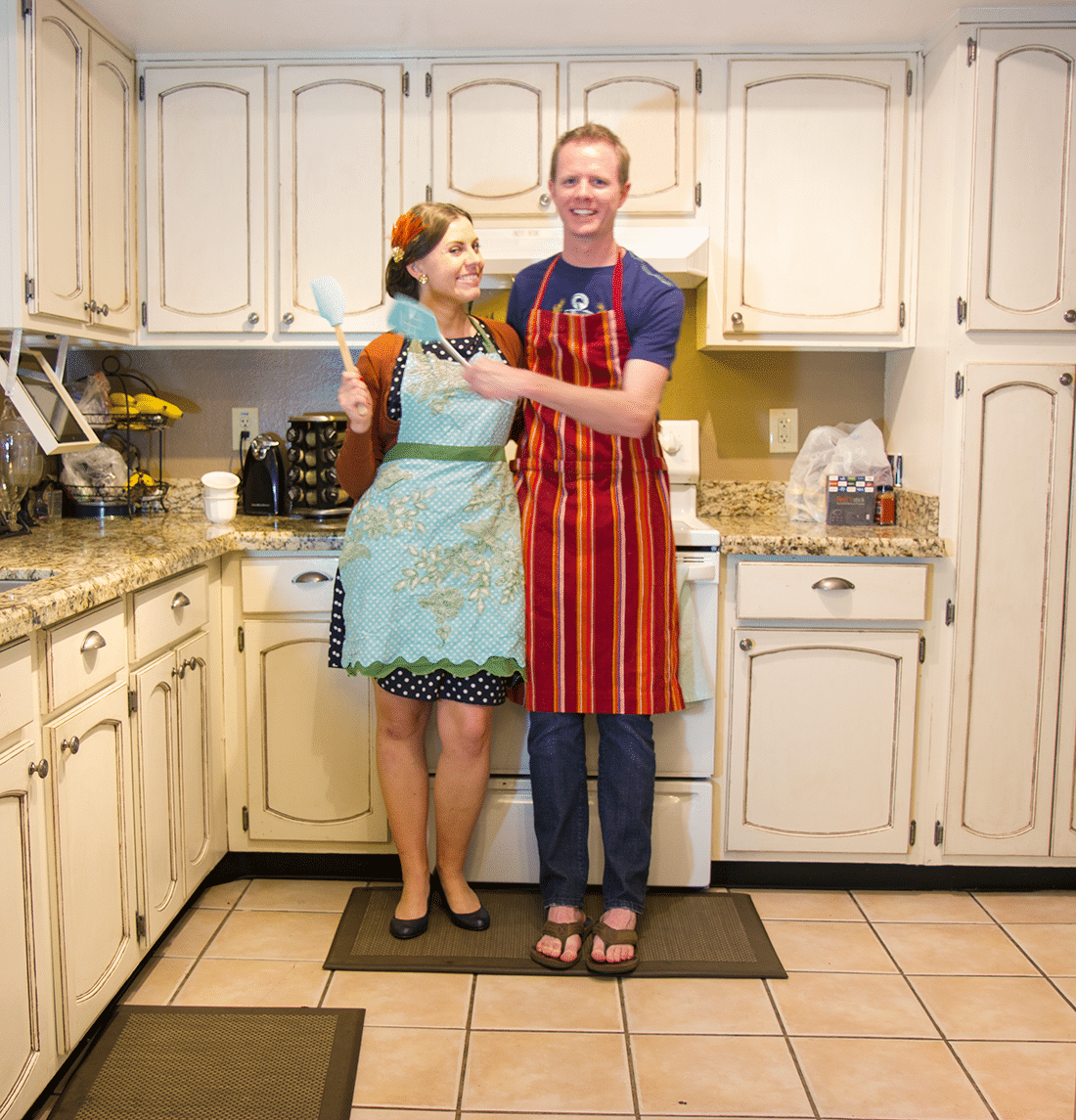 Couple standing in front of their kitchen stove cooking dinner at home together for date night in their aprons. 