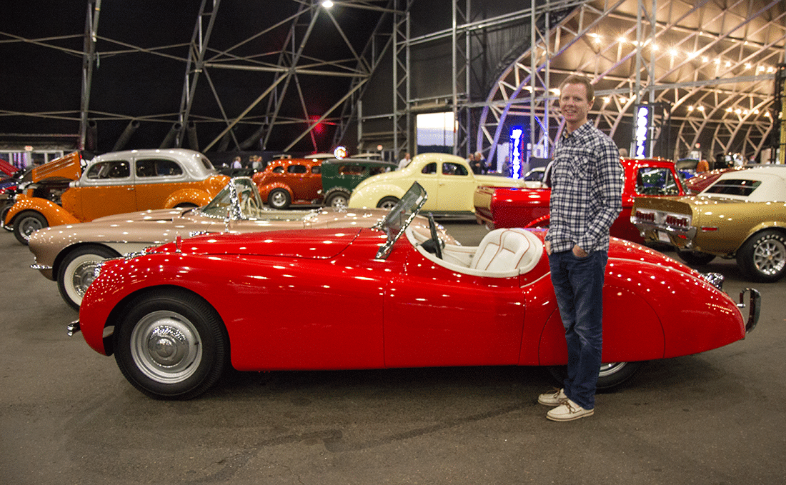 Man standing in front of red car at the Barrett Jackson auto show. 