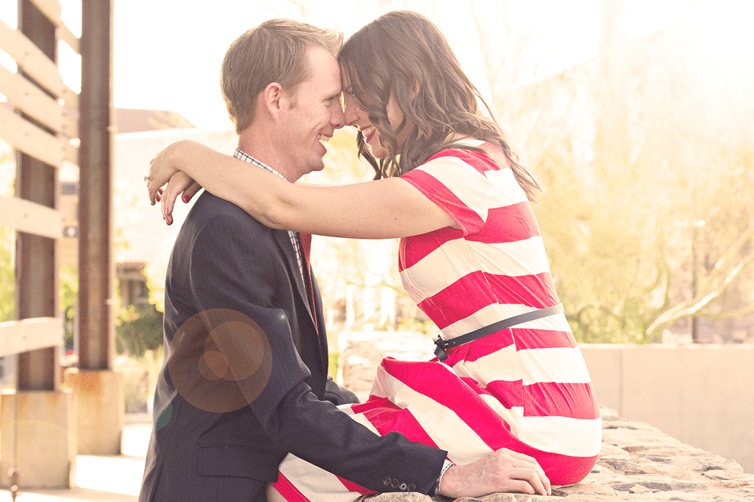 Wife sitting on a fence with husband standing next to her for a cute anniversary couples picture. 