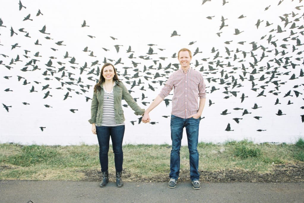 A couple holding hands in front of a mural. 