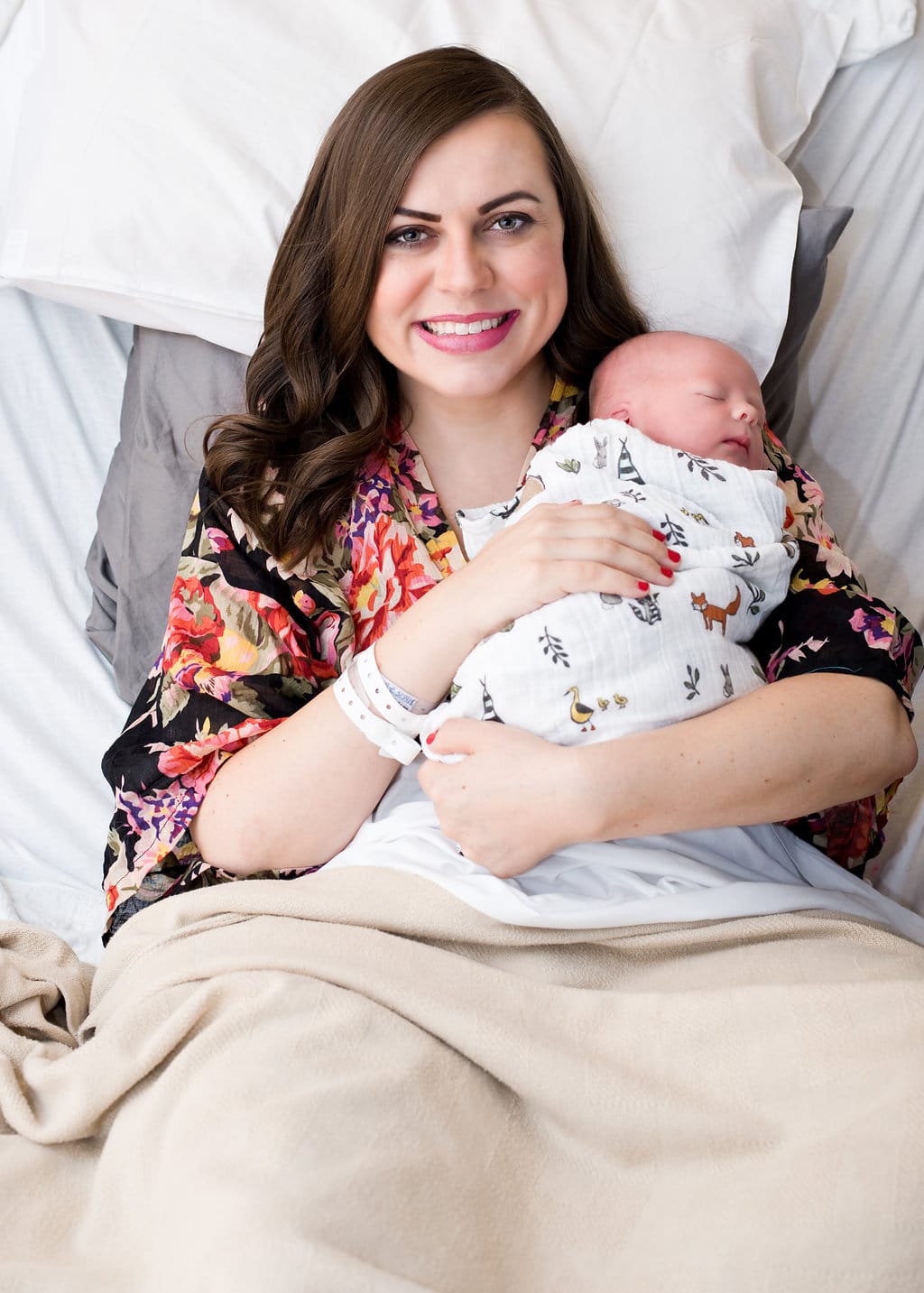 Newborn baby photo shoot in hospital: New mom in hospital bed snuggling swaddled newborn baby. 