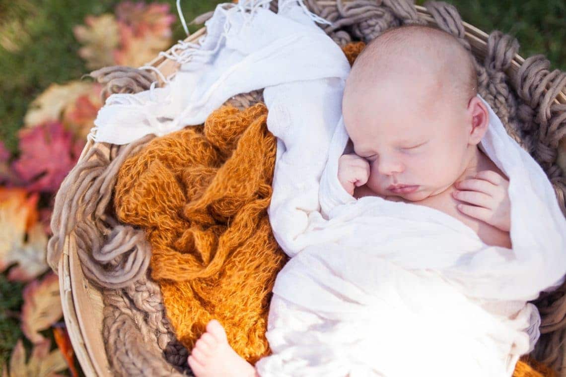 Swaddled newborn baby in a basket for a newborn photo shoot. 