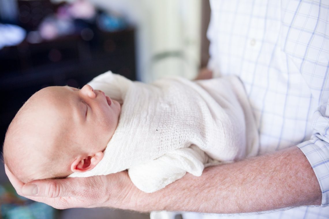 Swaddled newborn baby with dad holding in forearm. 