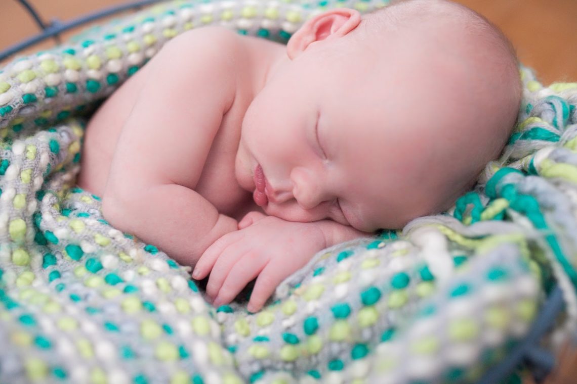 Newborn baby photo shoot with baby asleep in a colorful blanket. 