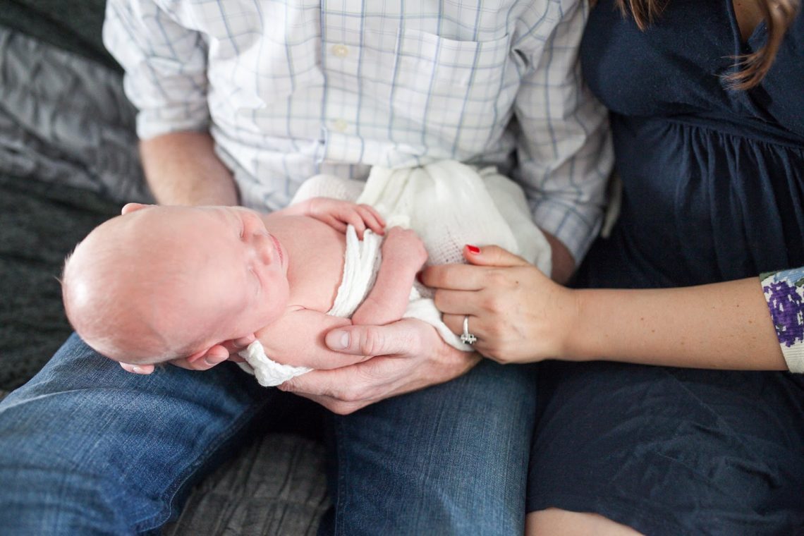 Swaddled newborn baby being held by mom and dad. 