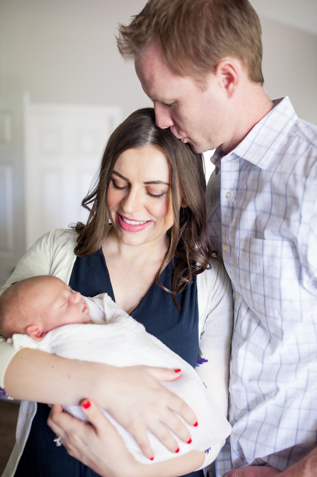 New parents holding their swaddled newborn baby for newborn photo shoot session at home. 