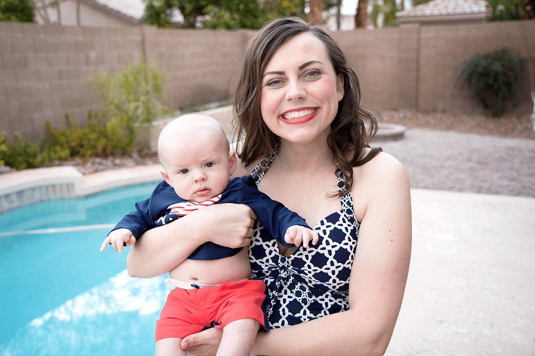 Mom holding new baby in Target swimsuits next to a swimming pool. 