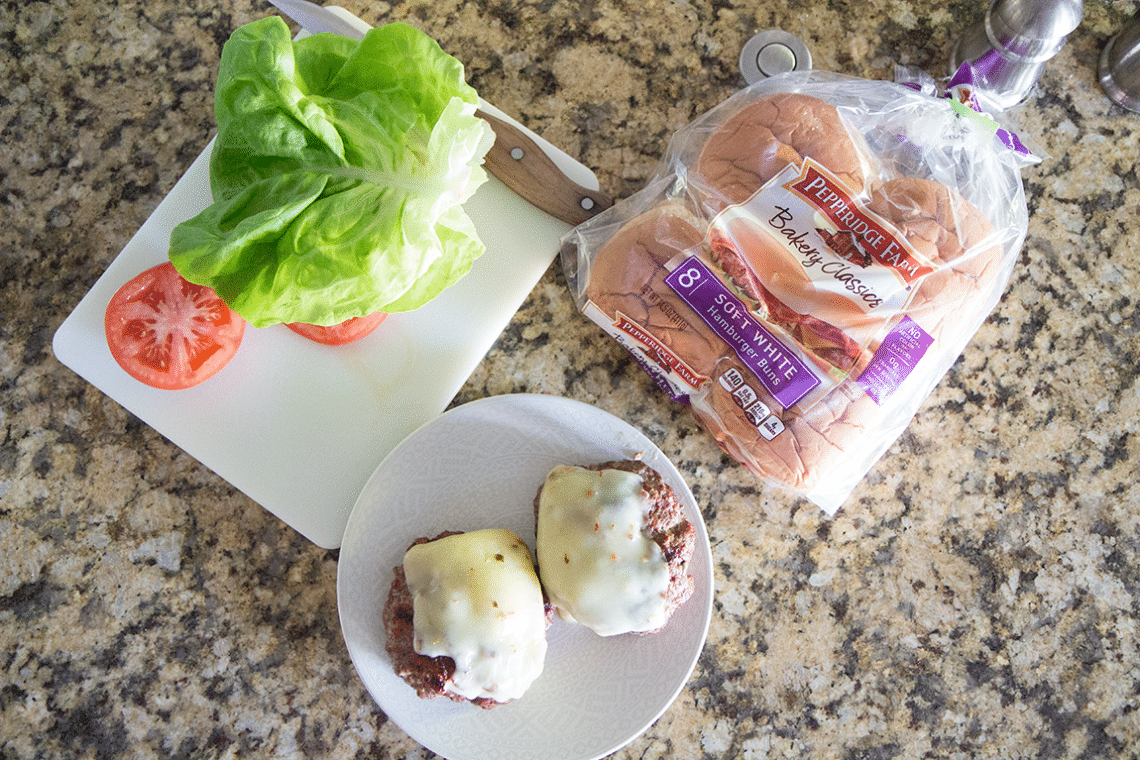 Jalapeno burger patties next to cut lettuce and burger buns. 