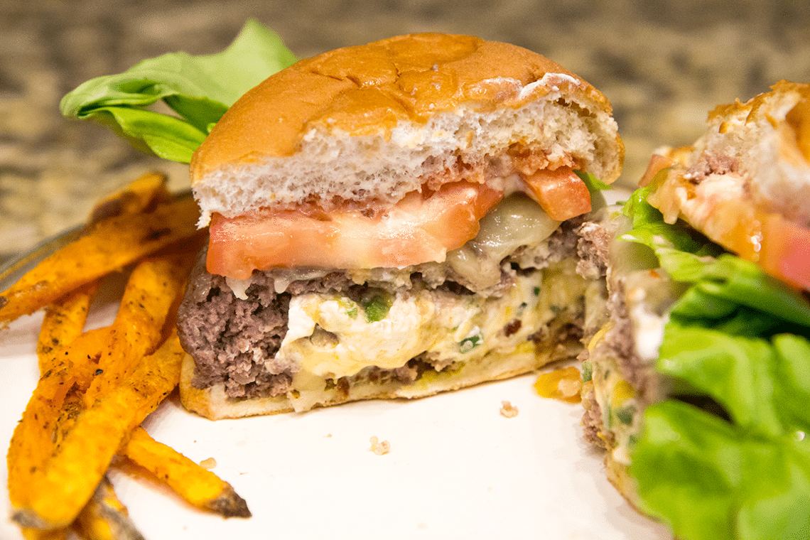 Jalapeno popper burger cut in half with cheese oozing out. 