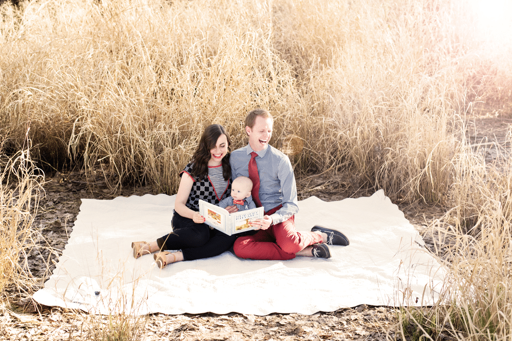 Couple on a picnic blanket reading to their toddler. 