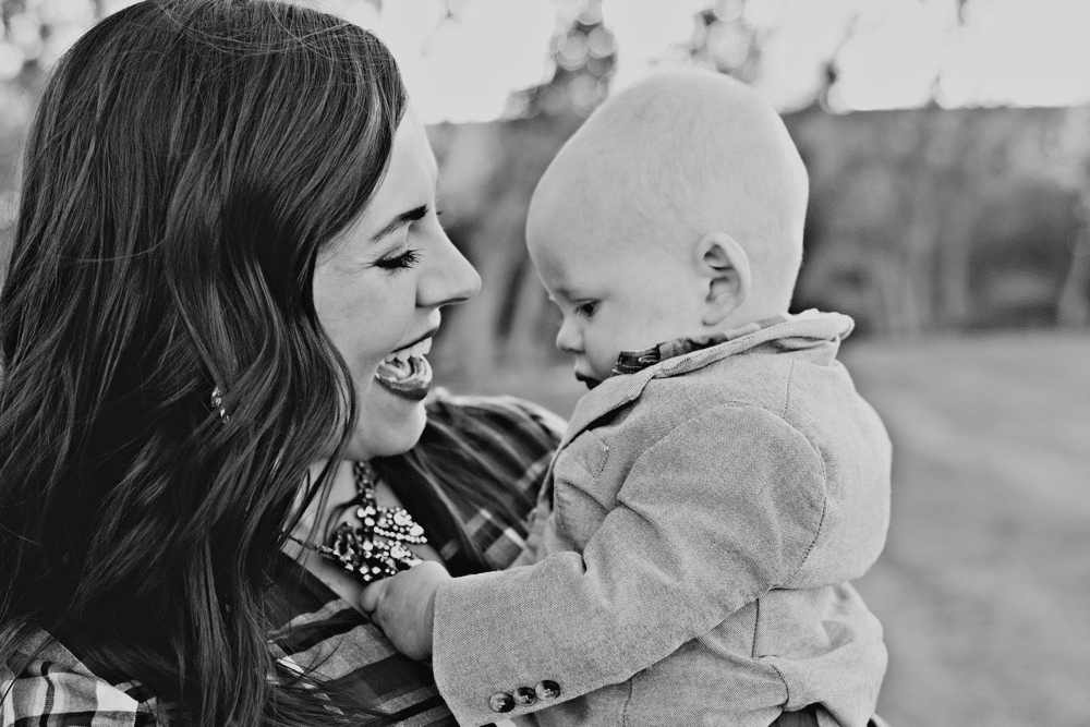 Young mom holding an infant who is playing with her necklace. 