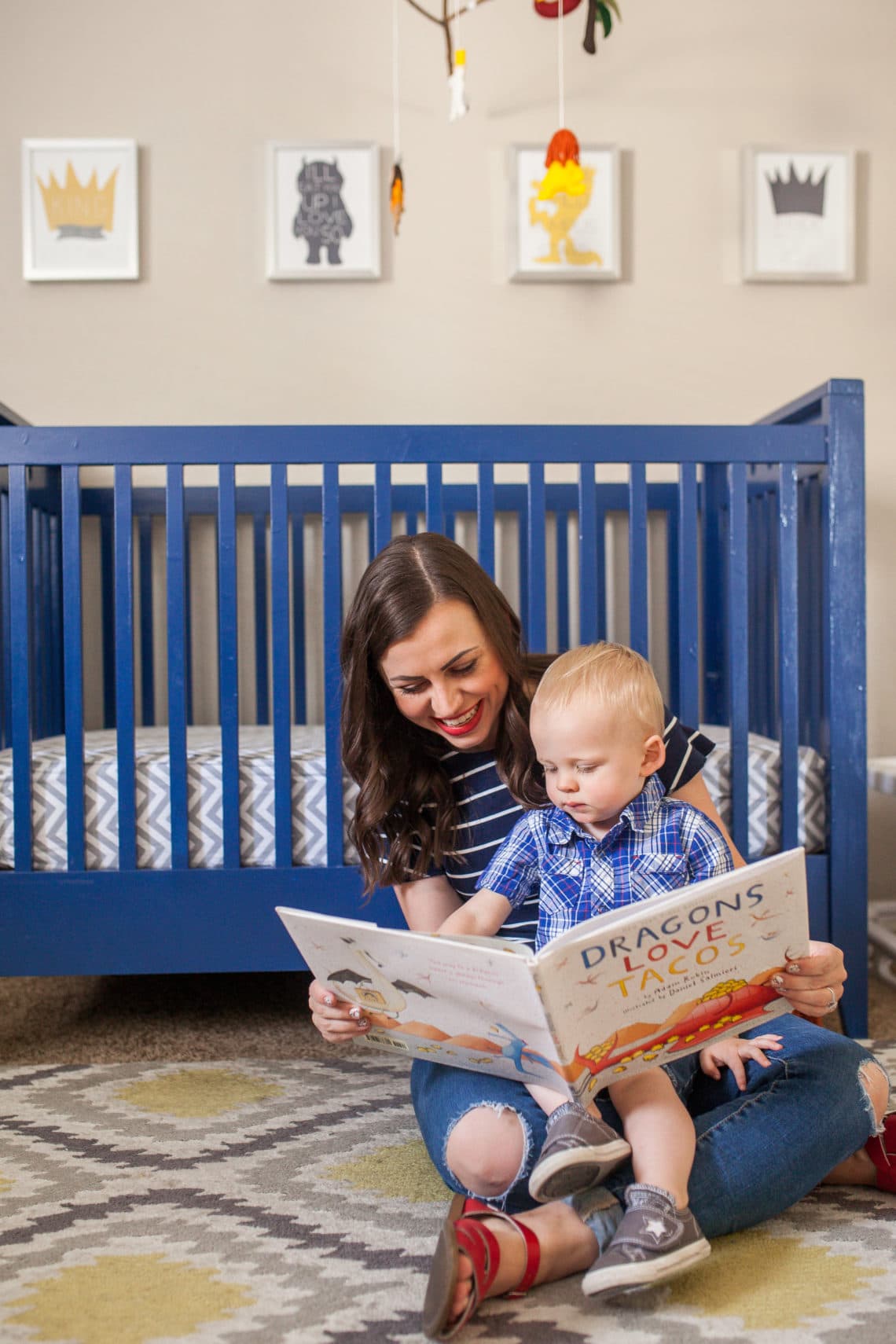 Mom reading to toddler in front of a blue crib. 