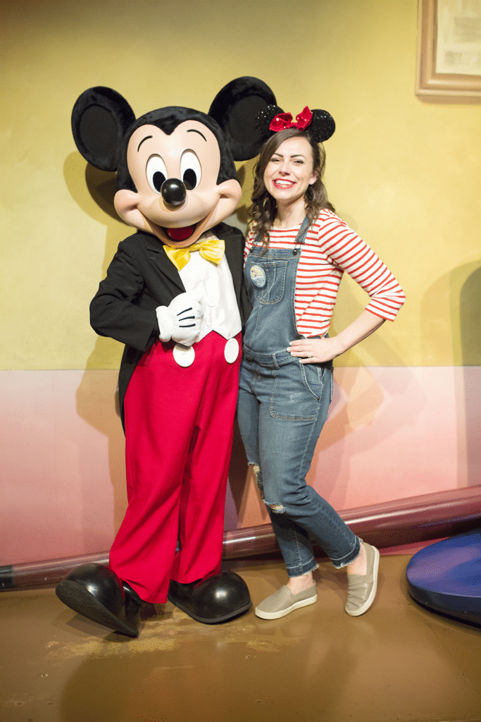 A woman pregnant at Disneyland Posing with Mickey Mouse showing off the baby bump. 