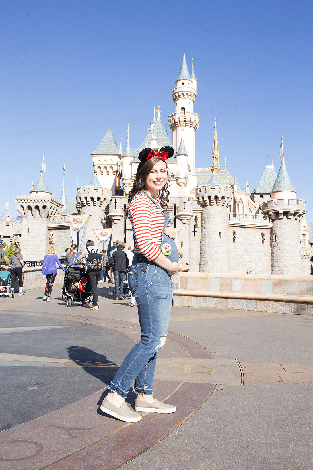 An expecting mom pregnant at Disneyland standing in front of the Disneyland castle. 