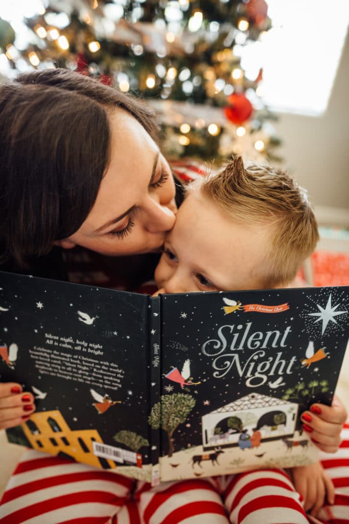 Mom reading Christmas books for kids next to the Christmas tree. 