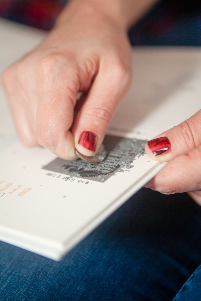 A close up on a hand Doing a scratch off date night from The Adventure Challenge. 