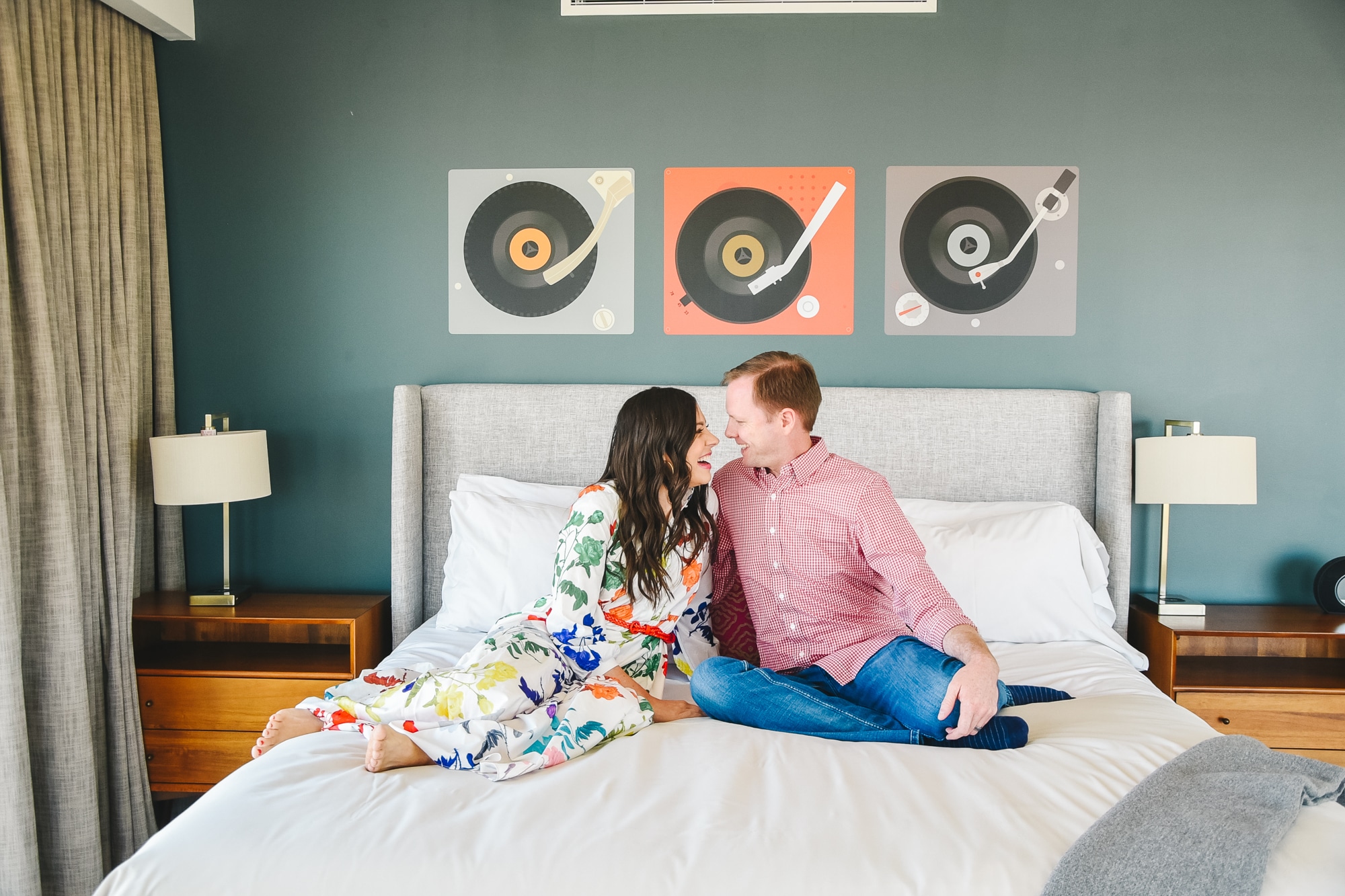 Couple sitting an a bed in a hotel room getting ready for a hotel date night. 