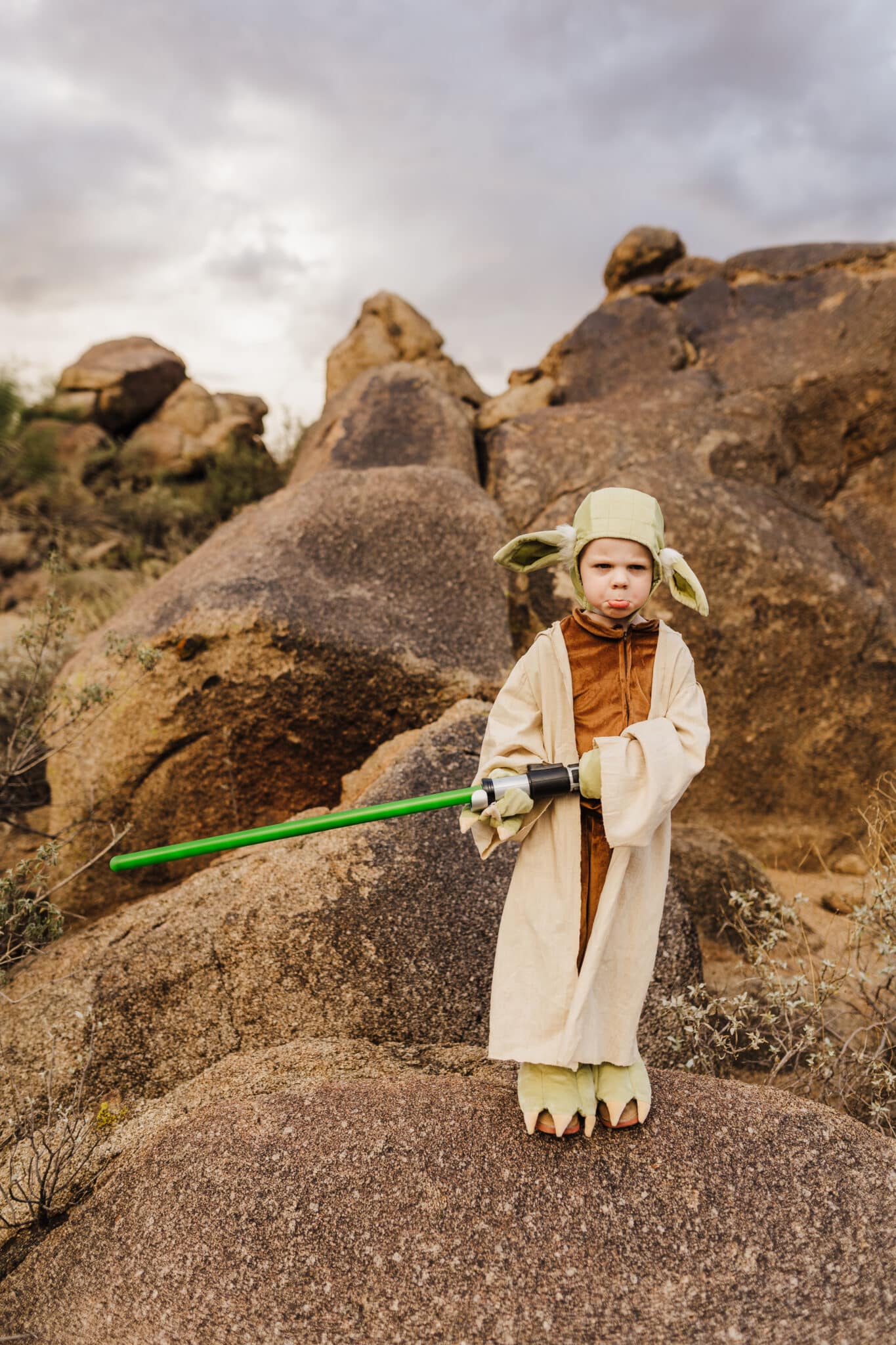 A kid standing in the desert on rocks showing his Yoda Costume for Kids. 