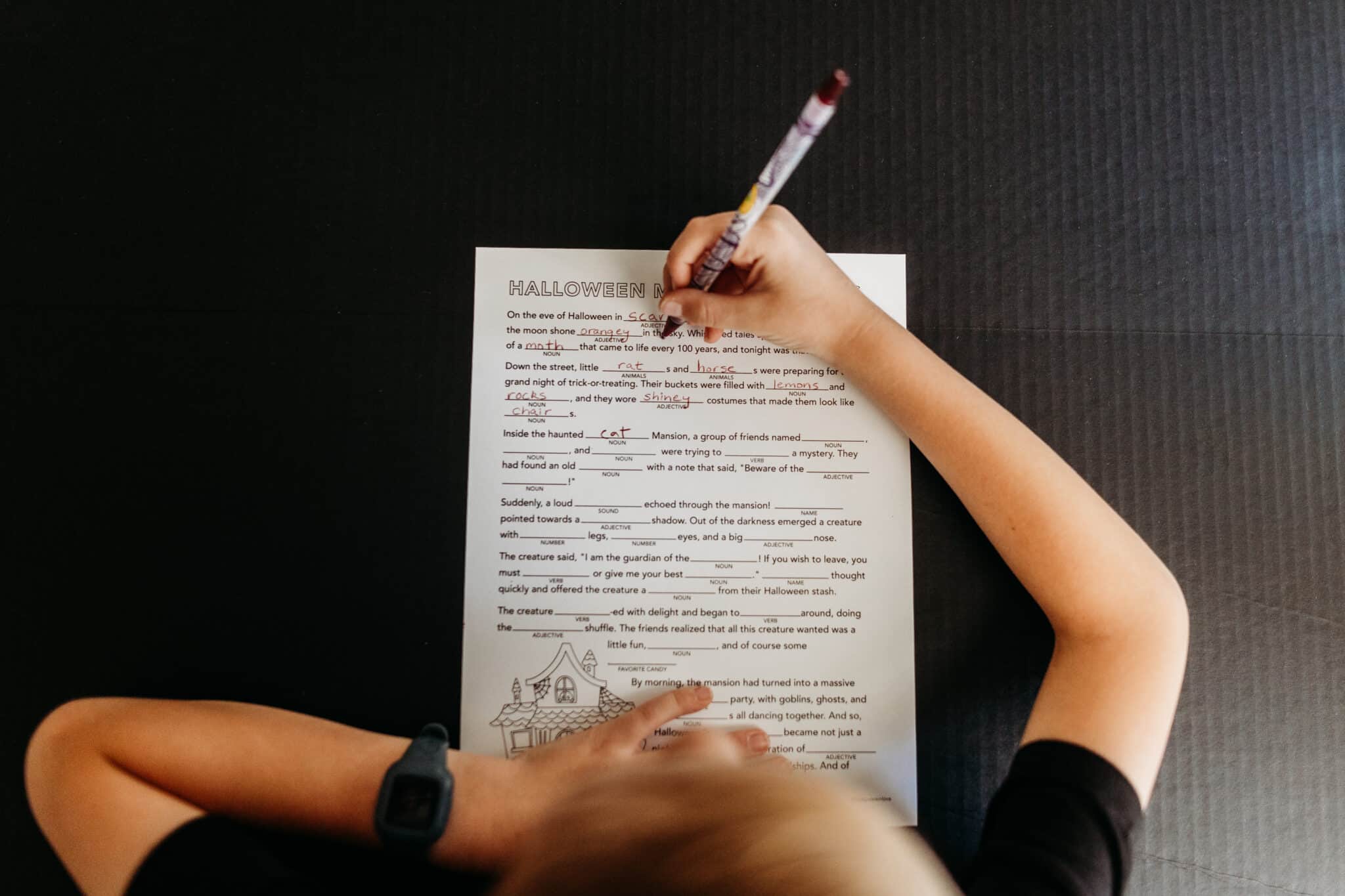 Child filling out a Halloween Mad Libs Printable. 