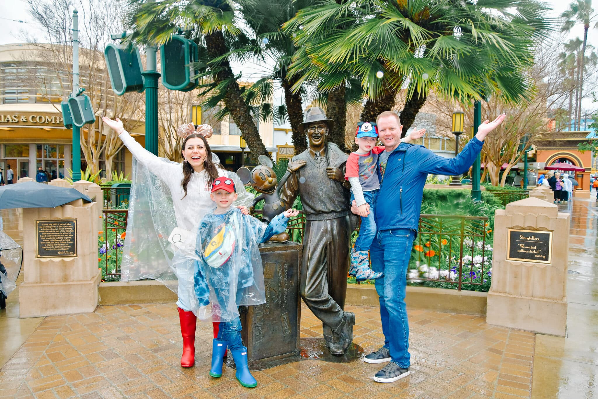 A family standing next to Walt statue enjoying Disneyland in the rain. 