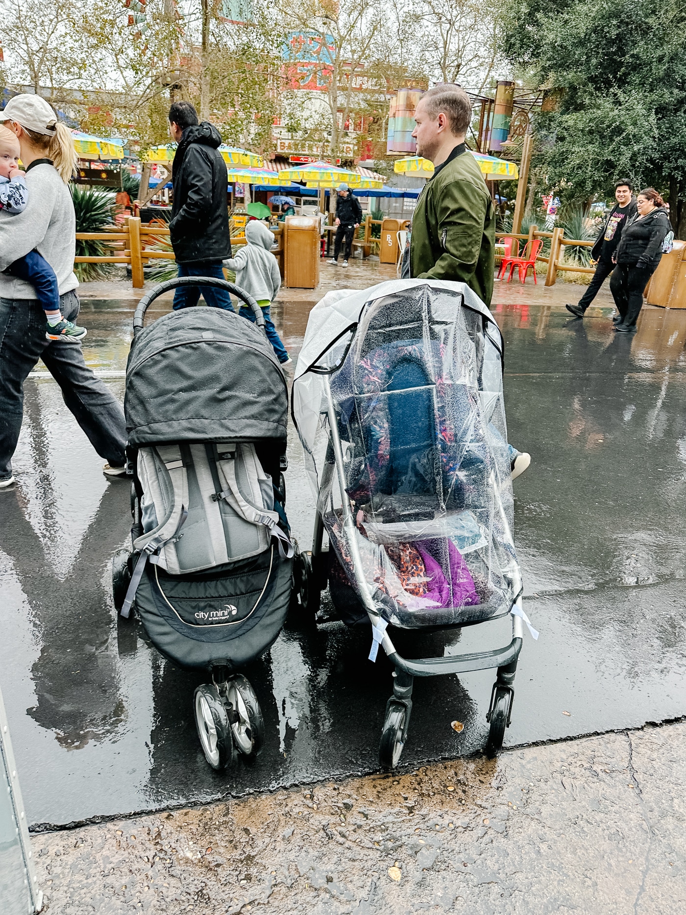 Rainy day at Disneyland with strollers side by side showing a rain stroller cover and a wet stroller without one. 
