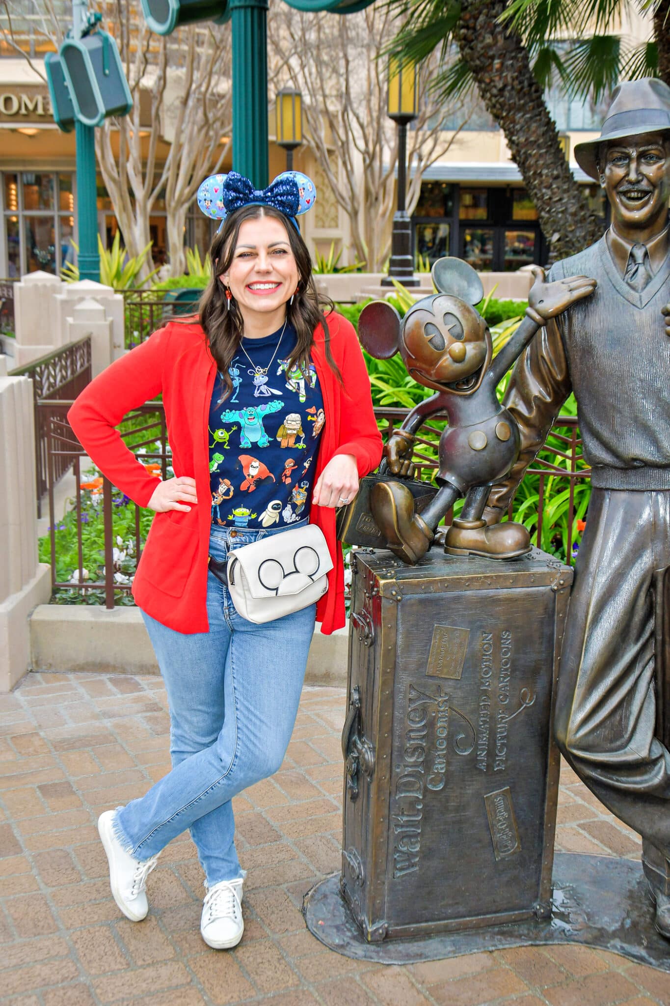 Disneyland outfits for women wiht a woman modeling a Disney shirt, jeans, a cardigan, and Mickey ears. 