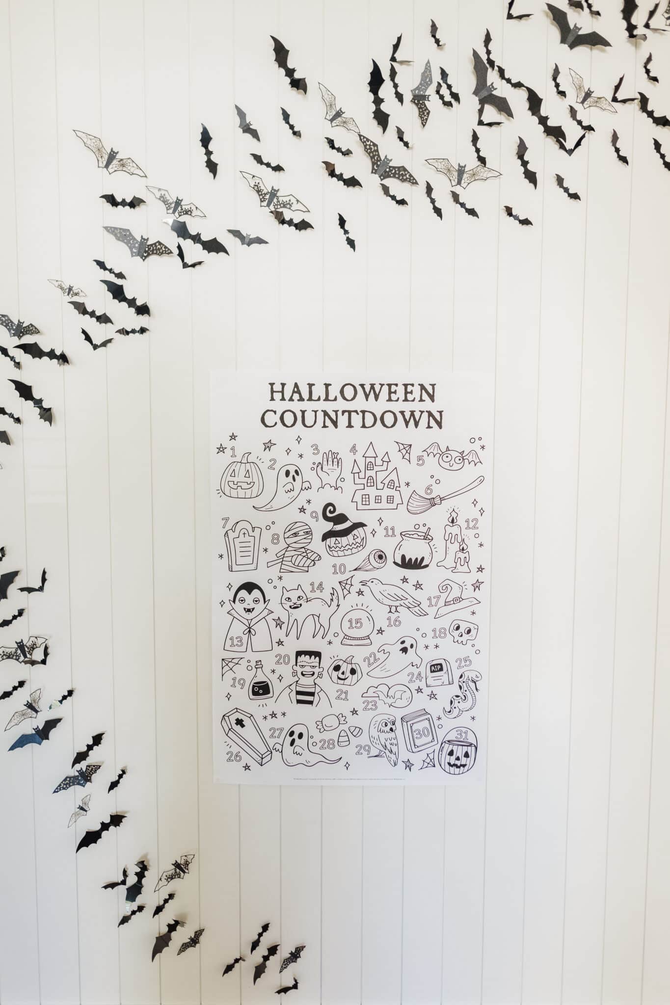 Halloween Advent Calendar free printable on a white wall with paper bats flying around it. 